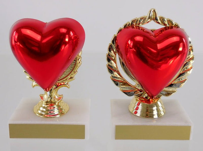 Two heart-shaped trophies with a glossy red heart figure on a gold-colored stand, one larger and one smaller, both on a white base.